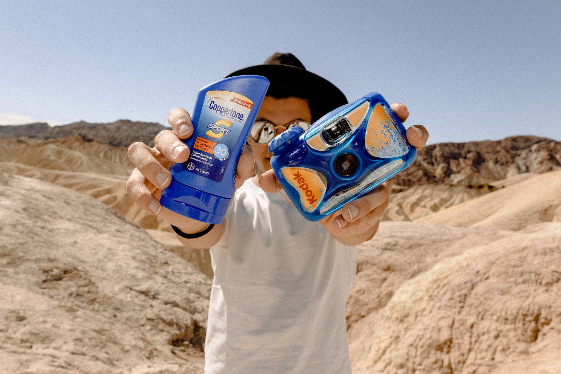 man holding blue kodak camera and sunscreen