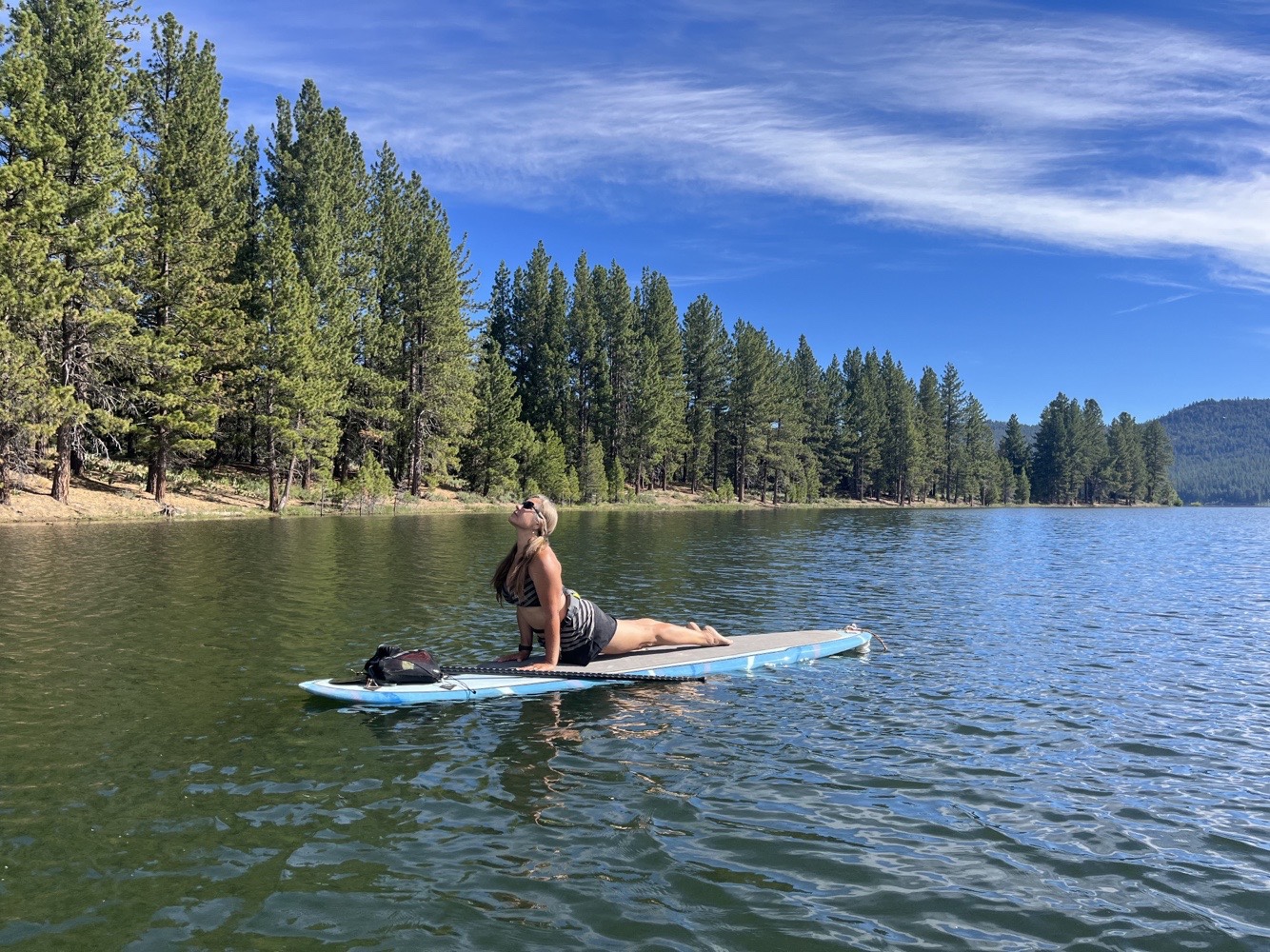 Woman on paddle board on lake in an upward dog yoga posture. Blue skies with beautiful streaking clouds are in the background.